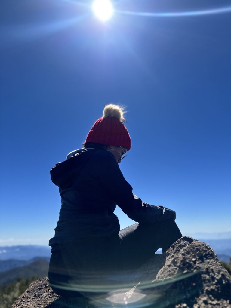 Persona con gorro rojo sentada en una roca bajo el sol brillante